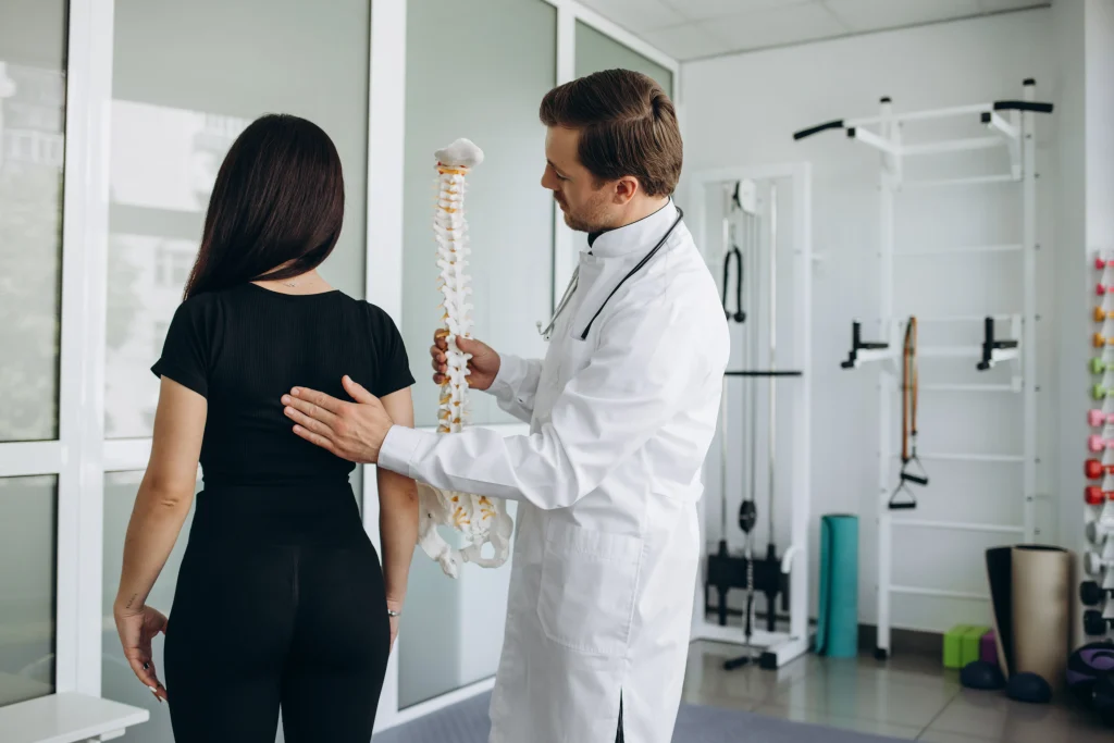 Doctor evalúa a mujer, enseñándole una maqueta de una columna, explicando la descompresión espinal