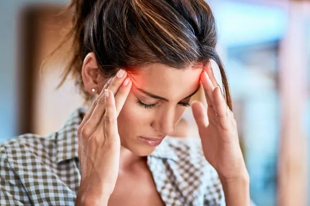 Mujer con la mano en la frente mostrando signos de migraña intensa y molestia persistente por Dolor de cabeza constante.