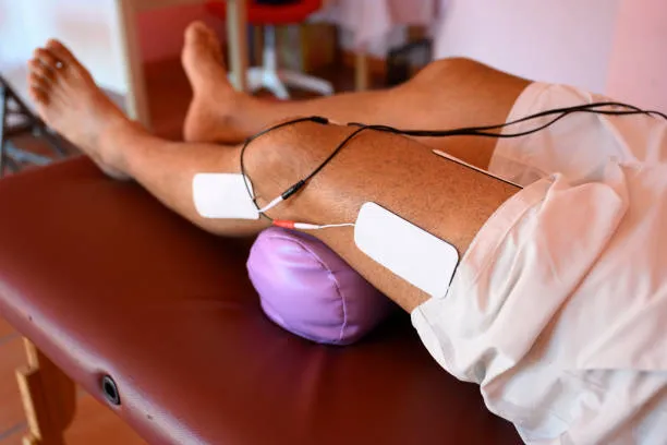 Hombre sentado recibiendo electroterapia aplicada en ambas piernas para estimular músculos, reducir dolor y mejorar movilidad usando electroterapia